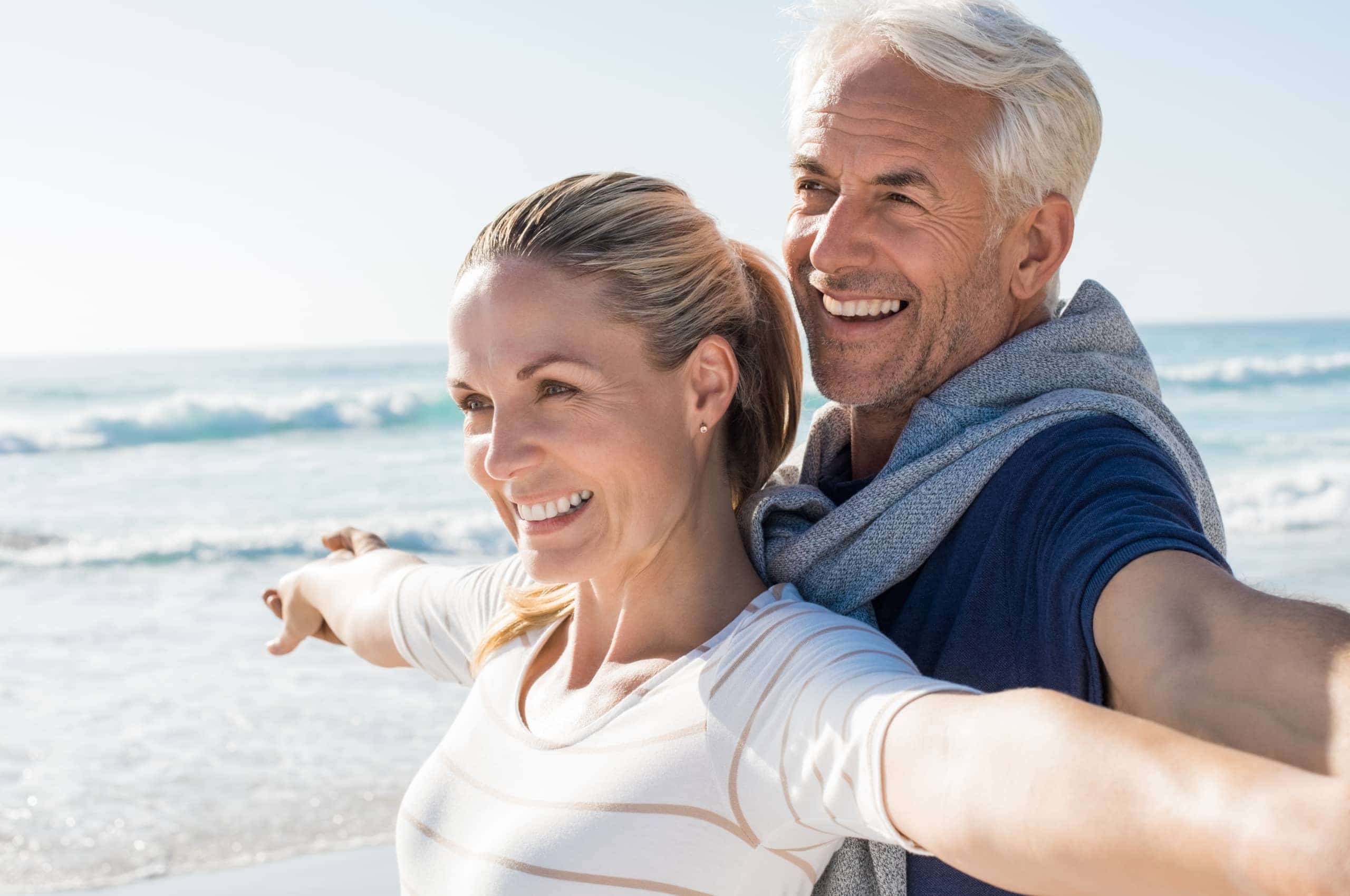 Happy,Senior,Couple,Standing,On,Beach,With,Arms,Outstretched,And