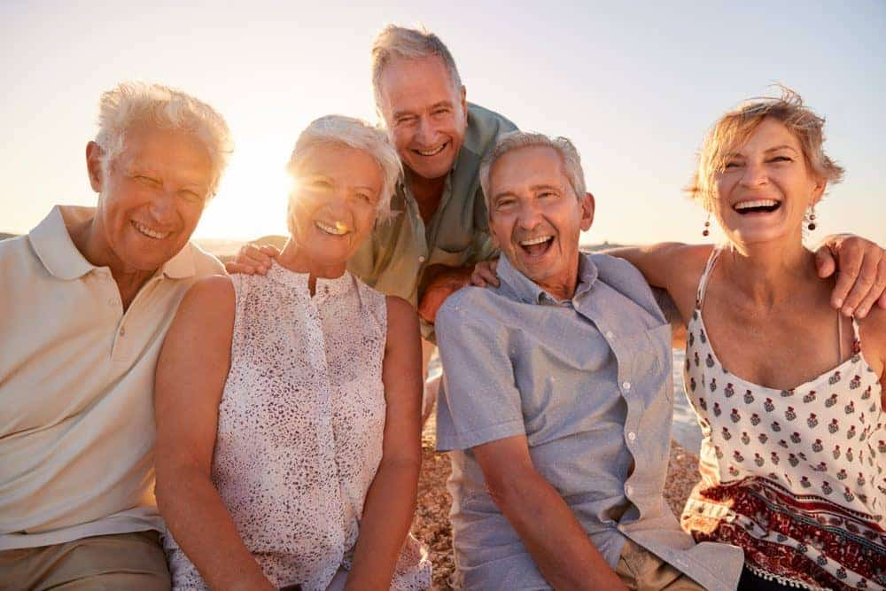 Portrait,Of,Senior,Friends,Sitting,On,Rocks,By,Sea,On