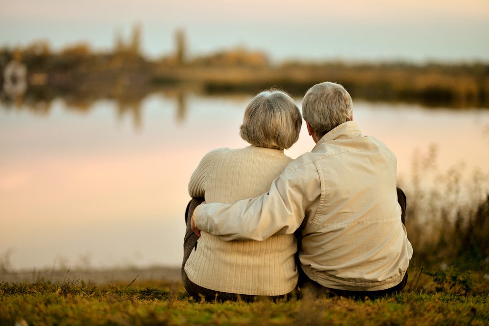 Happy,Senior,Couple,Sitting,In,Summer,Near,Lake,During,Sunset