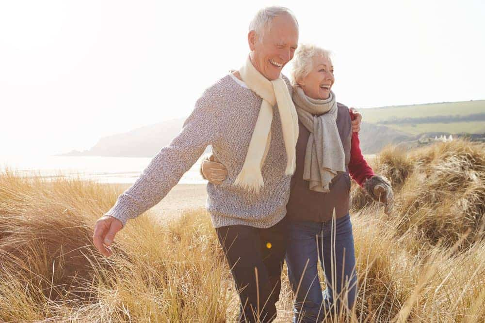 Senior,Couple,Walking,Through,Sand,Dunes,On,Winter,Beach