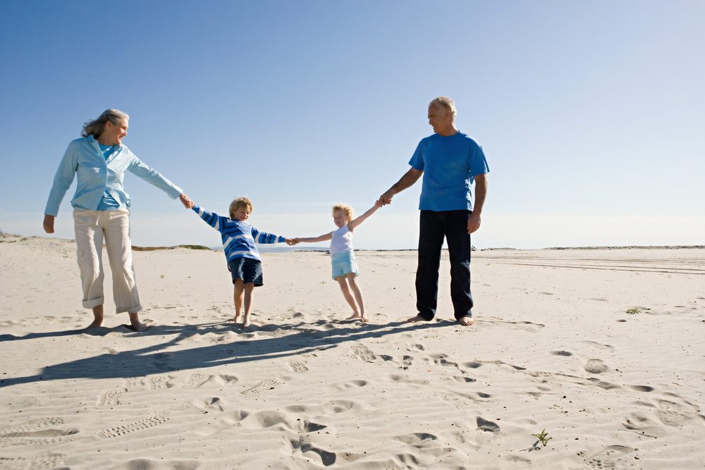 Grandparents,And,Grandchildren,Holding,Hands,,Walking,On,Beach